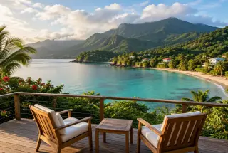 Baie tropicale de Guadeloupe avec plage turquoise, végétation dense et reliefs volcaniques visibles depuis une terrasse en bois.
