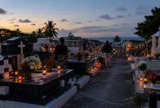 Cimetière guadeloupéen illuminé par des bougies à la tombée de la nuit, avec des fleurs et des visiteurs recueillis.